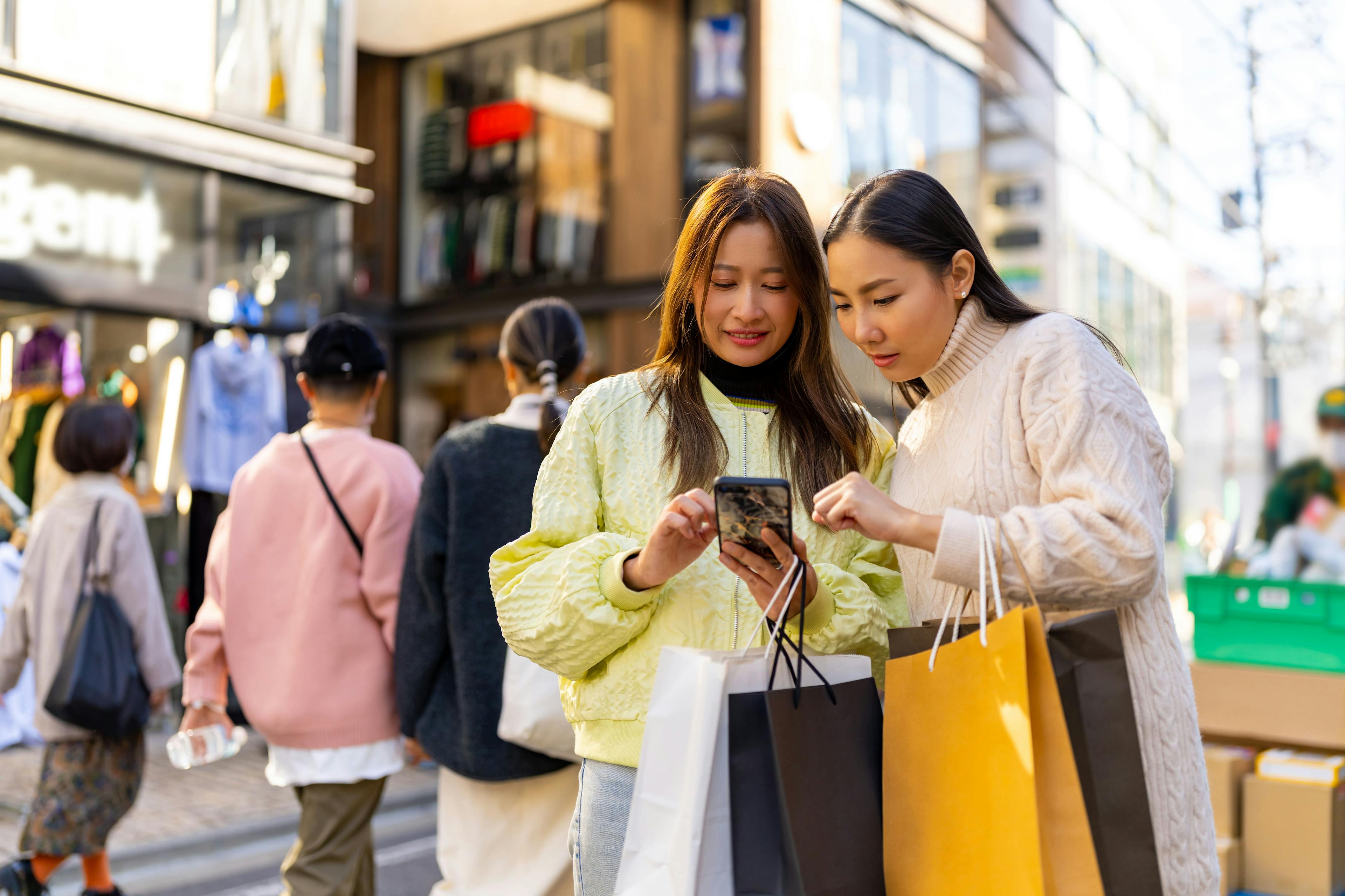 Asian women using mobile phone during shopping together at Shibuya district, Tokyo, Japan.