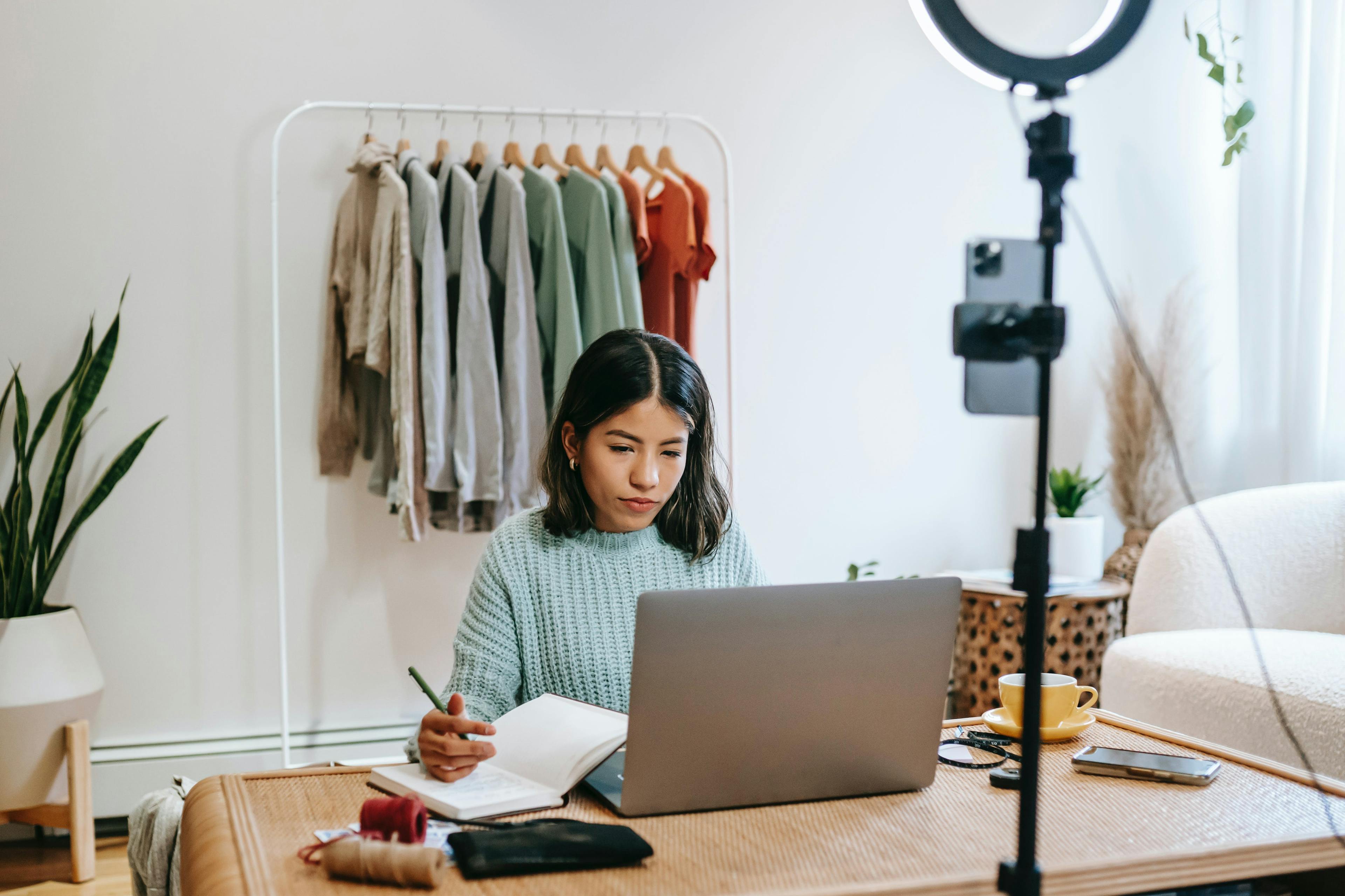 woman sitting at desk with laptop, smart phone, and ring light, as she works on social media content for her retail business