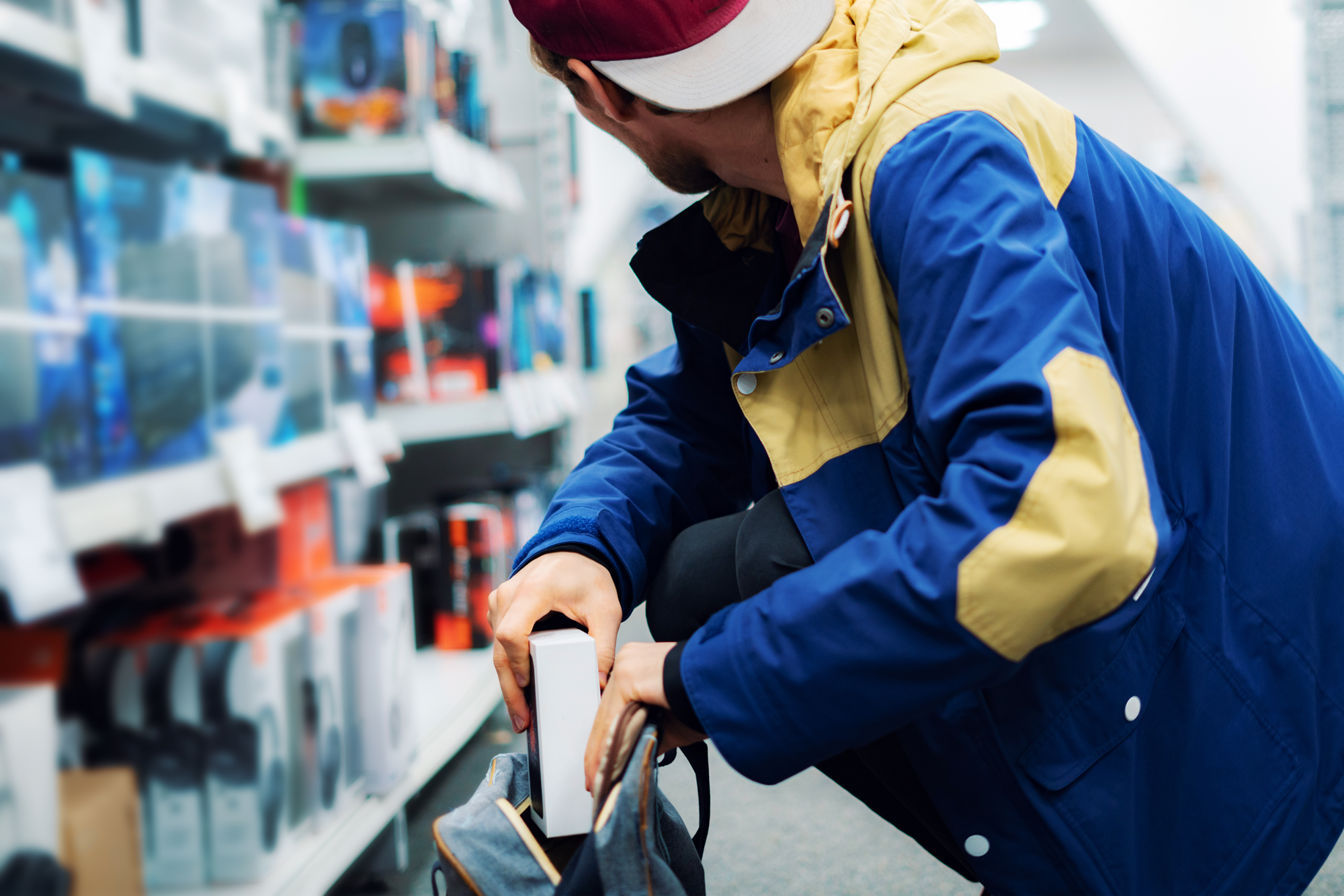 man in blue jacket in a store placing stolen goods into a bag 
