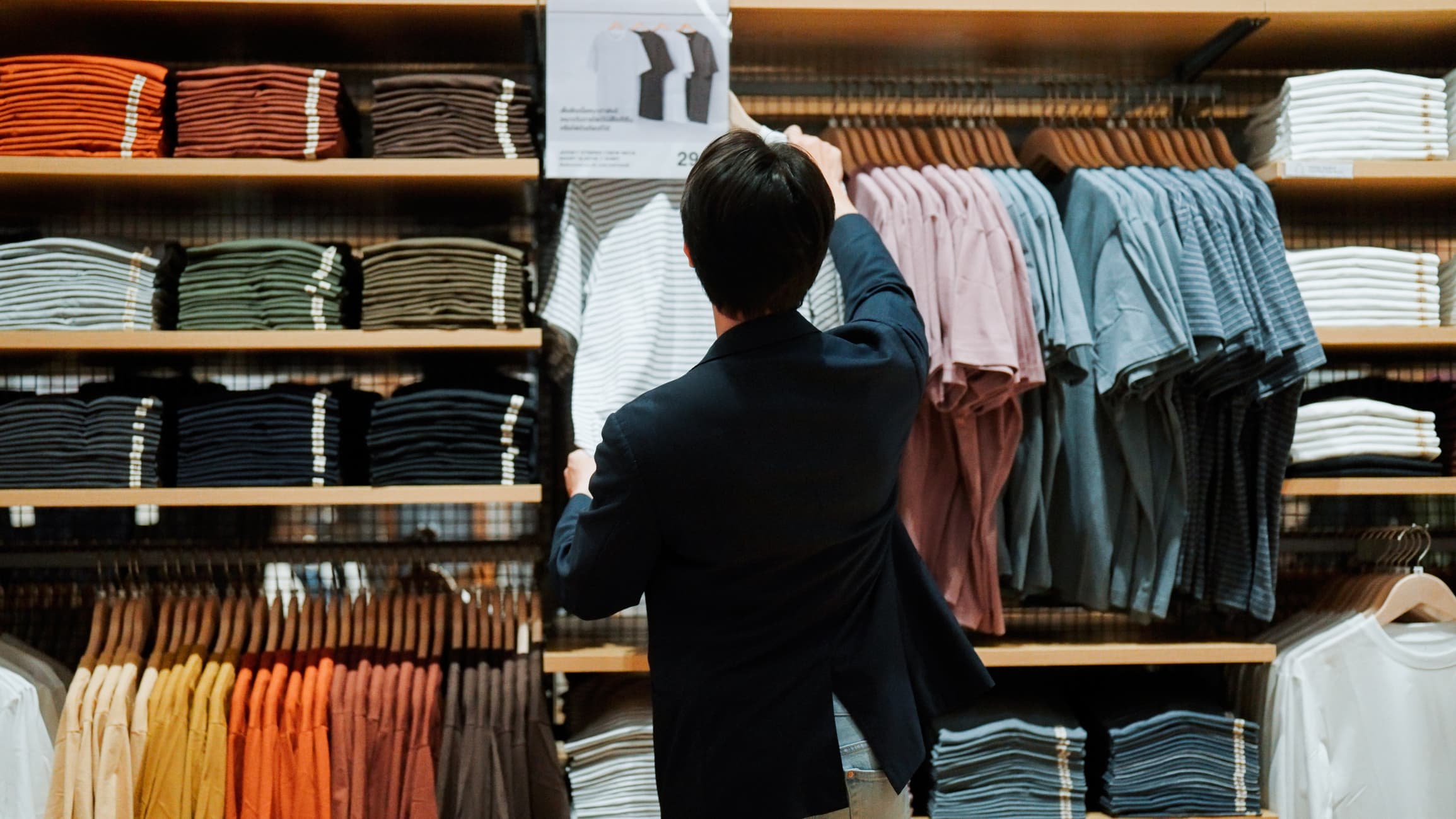 Young Asian man walking to a shelf and taking a t-shirt while shopping in a mall.