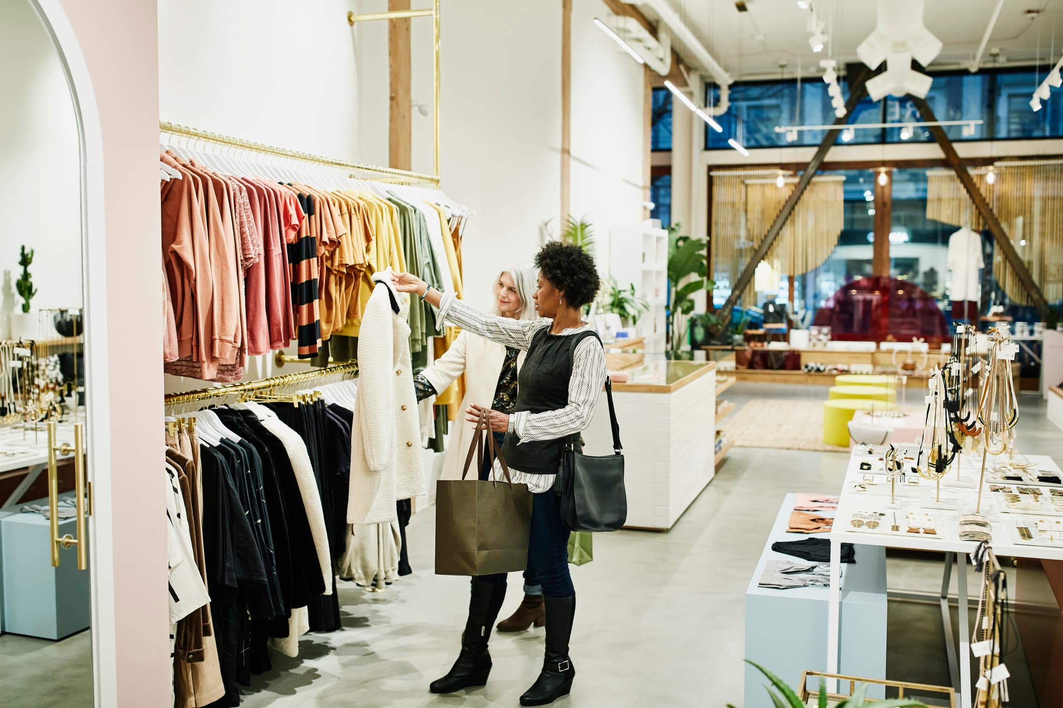 Mature female shoppers looking at coat while shopping together in clothing boutique