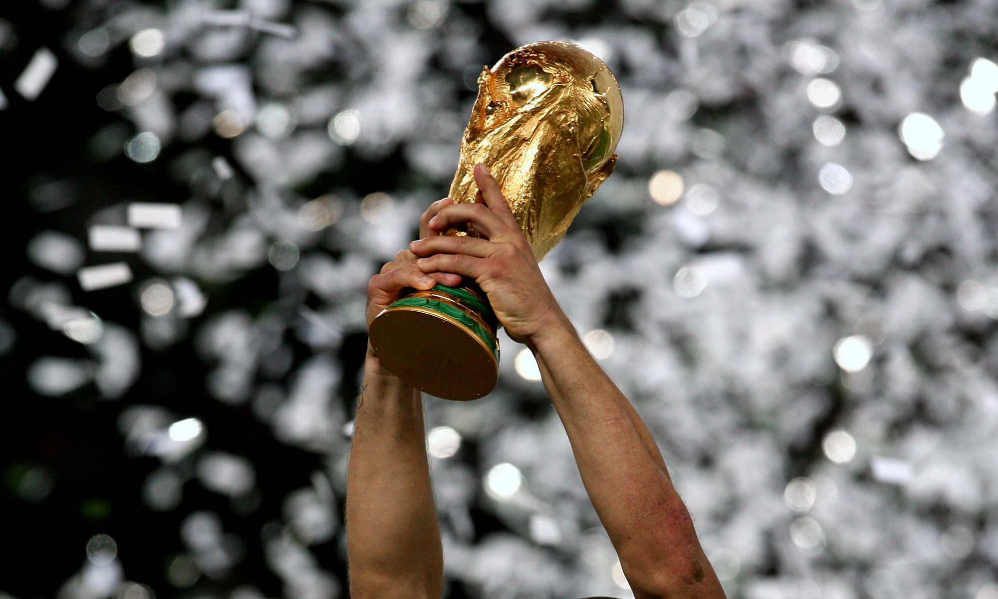 fifa world cup trophy held in the air with confetti in the background 