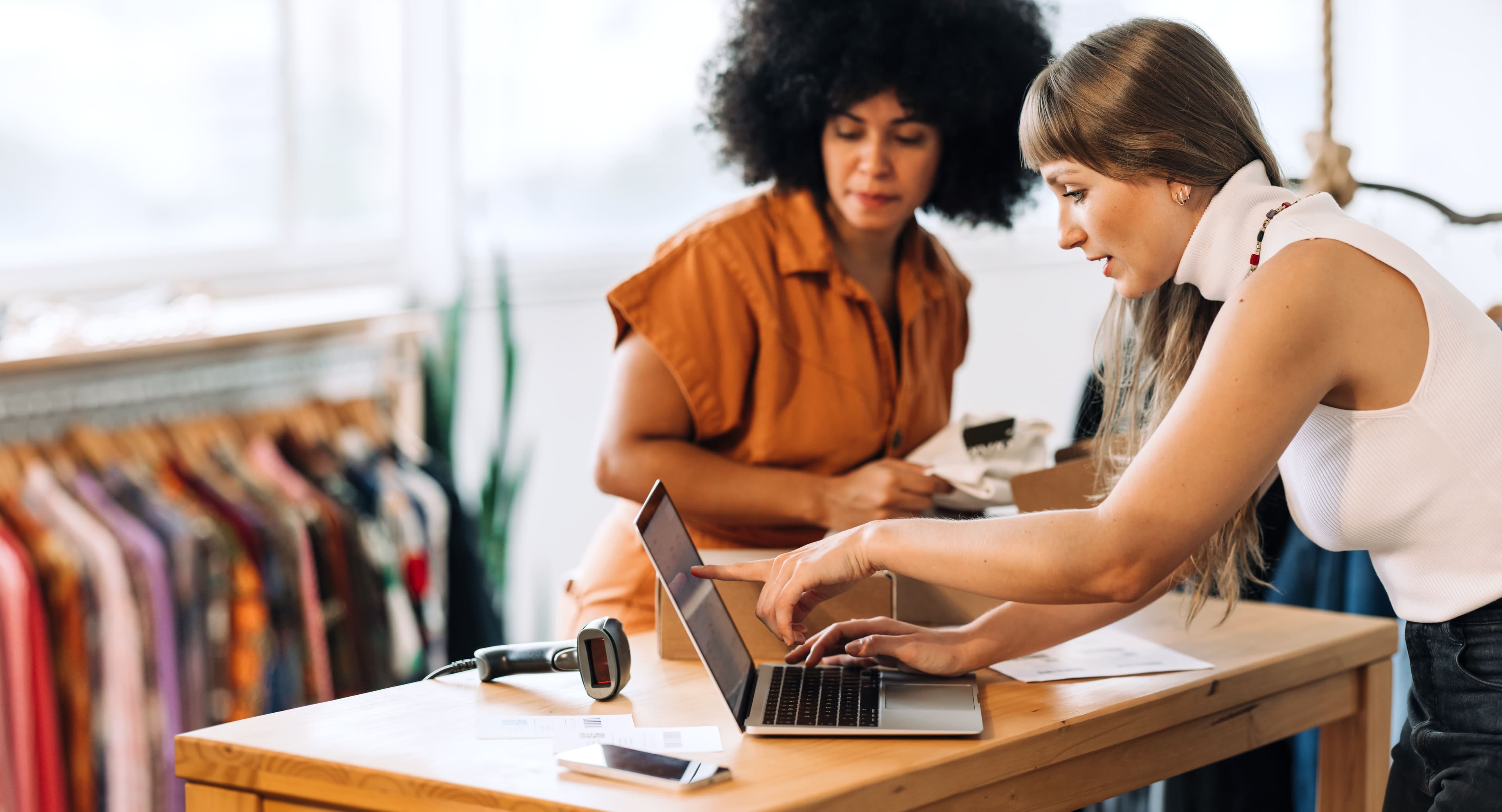 Two female store associates consult a tablet on the checkout