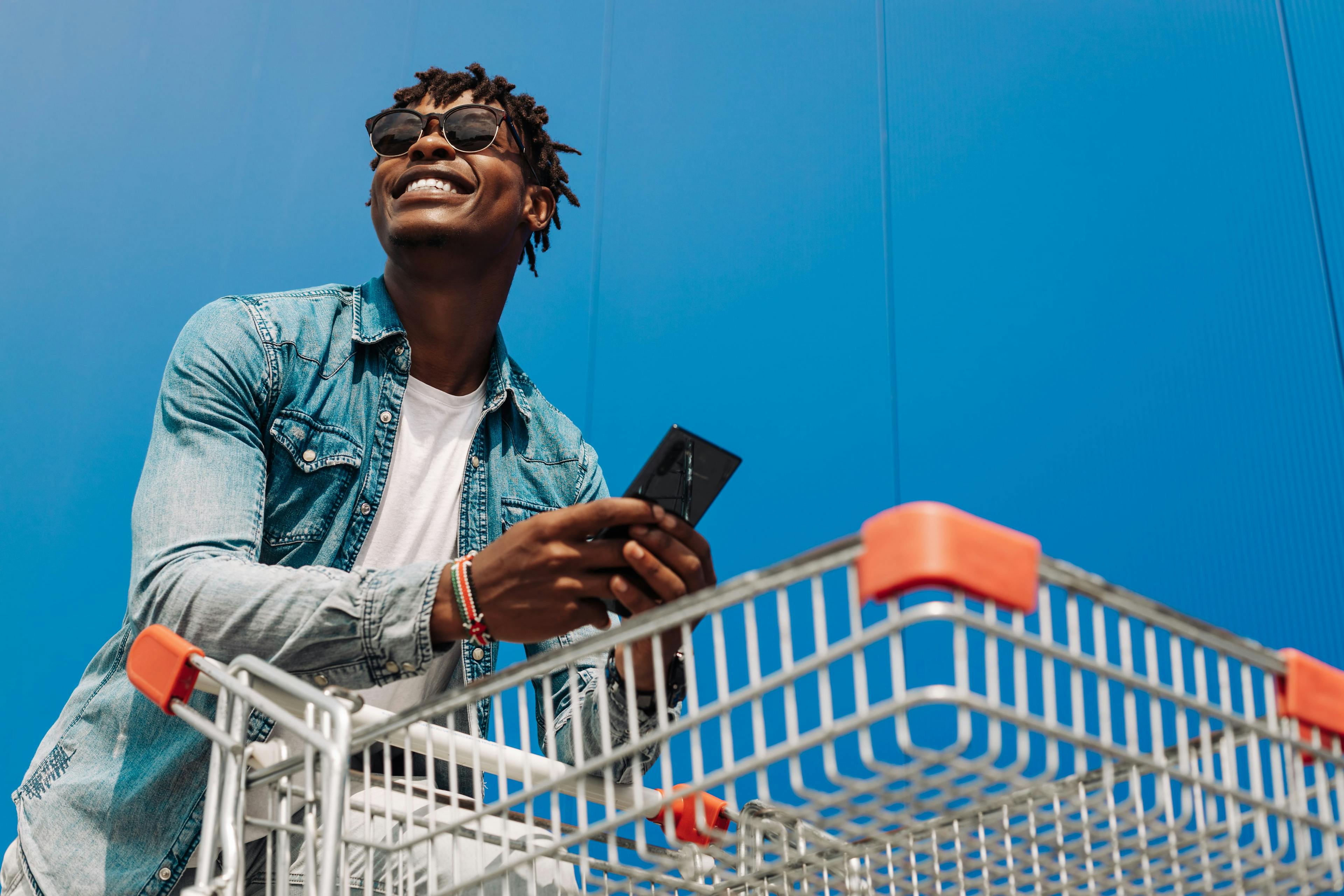 man with shopping cart holding phone in front of blue background 