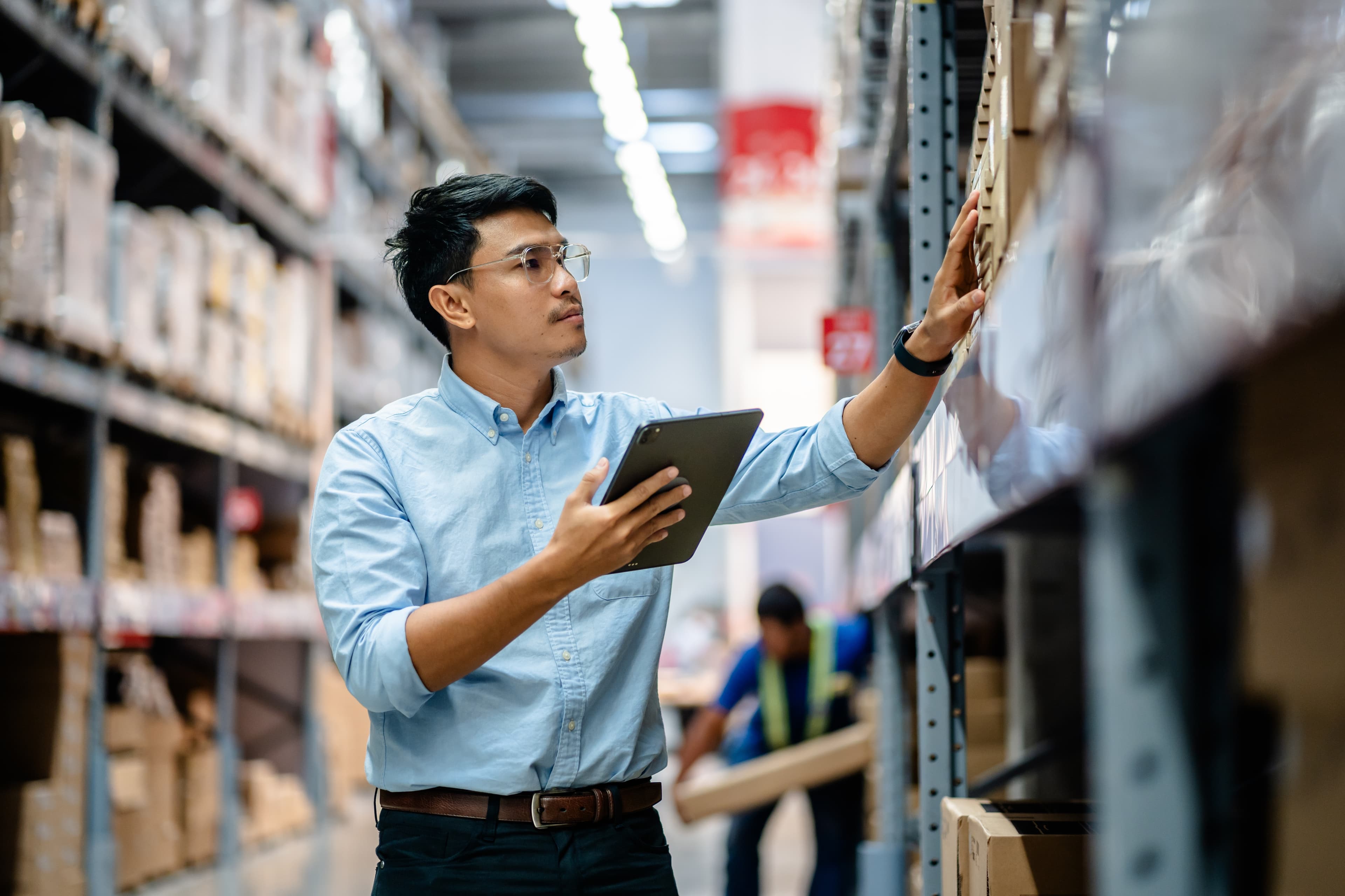 Businessman or supervisor uses a digital tablet to check the stock inventory on shelves in large warehouses, a Smart warehouse management system, supply chain and logistic network technology
