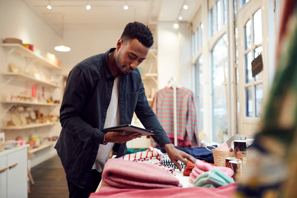 retail working holding an ipad is stocking fashion store shelves