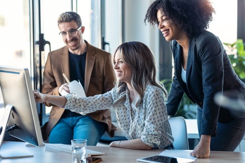 Successful business multiage team standing around computer for presentation of work 