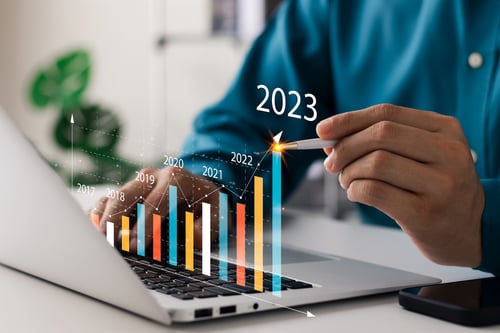 colourful bar graph of 2023 trends projected from a MacBook in front of a man wearing a blue shirt 