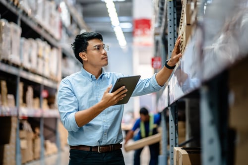 Businessman or supervisor uses a digital tablet to check the stock inventory on shelves in large warehouses, a Smart warehouse management system, supply chain and logistic network technology