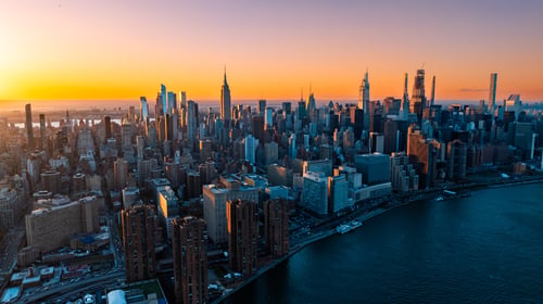 Orange light of setting sun illuminating the skyscrapers and high-rise buildings in New York scenery. Top view on the metropolis from above the East River.