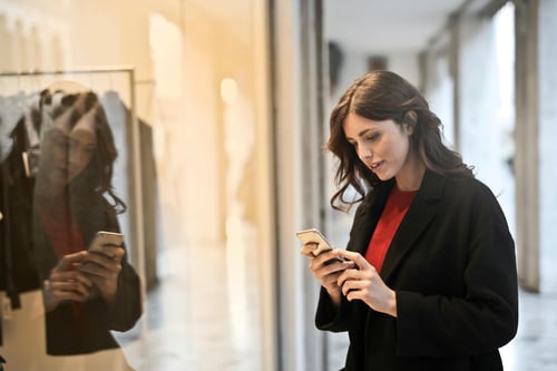 Close-up Photo of Woman in Black Coat Using Smartphone In Mall