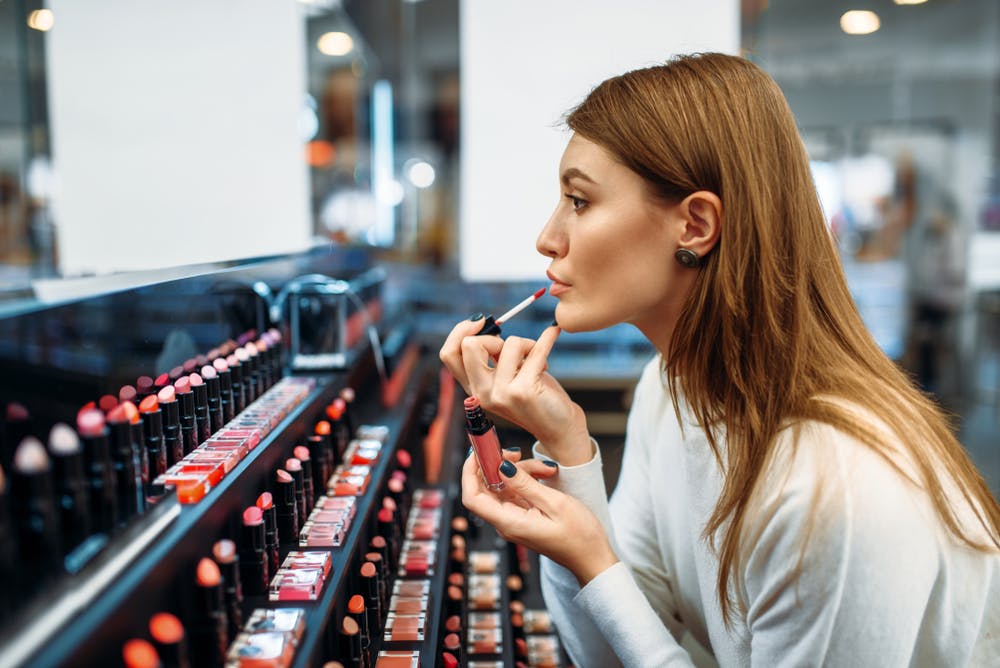 Female customer testing lip gloss in make-up shop